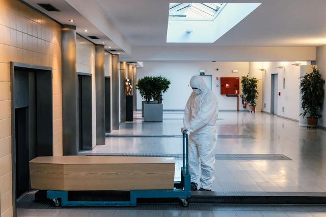 A worker, wearing a personal protective equipment (PPE), carries a coffin in the cremation of coronavirus victim at the Wilrijk crematory in Antwerp