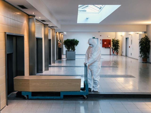 A worker, wearing a personal protective equipment (PPE), carries a coffin in the cremation of coronavirus victim at the Wilrijk crematory in Antwerp