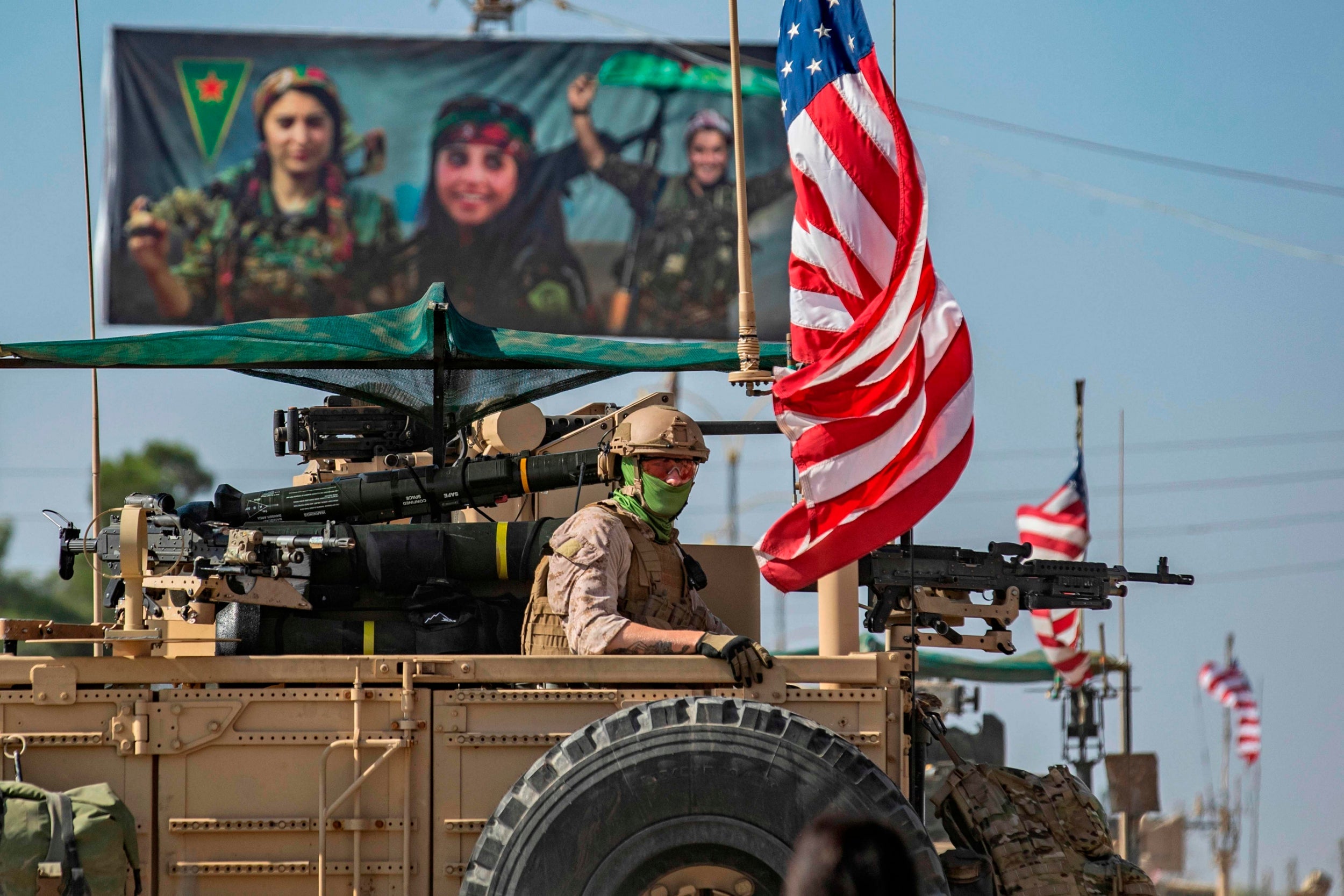 A US armoured vehicle drives past a billboard for the Syrian Kurdish Women’s Protection Units (YPJ) (AFP/Getty)