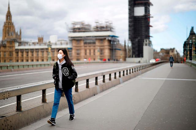 A woman wearing a face mask as a precautionary measure against Covid-19 walks across a deserted Westminster Bridge in London