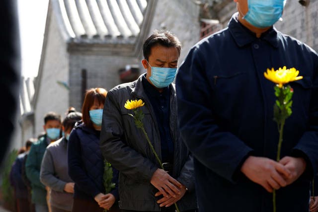 People holding flowers observe a moment of silence at a memorial event in Beijing for those lost to the coronavirus pandemic