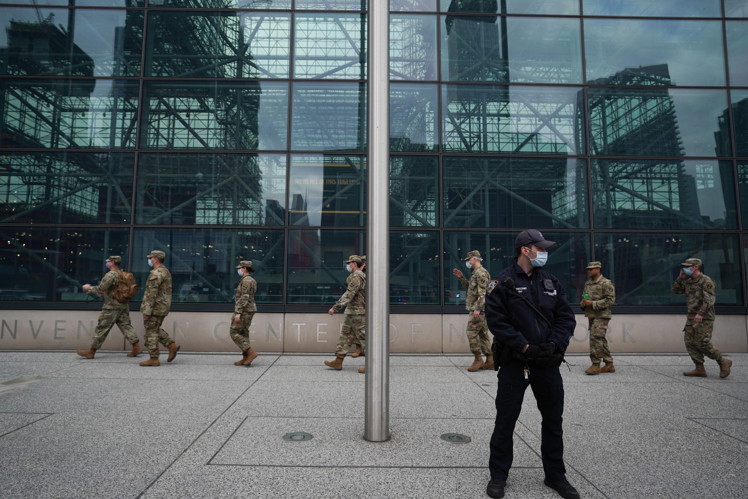 US Army National Guard members walk past a police officer wearing a mask outside of the Jacob K Javits Centre