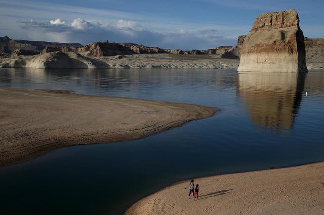 <p>People walk on a beach the used to be the bottom of Lake Powell at Lone Rock Camp</p>