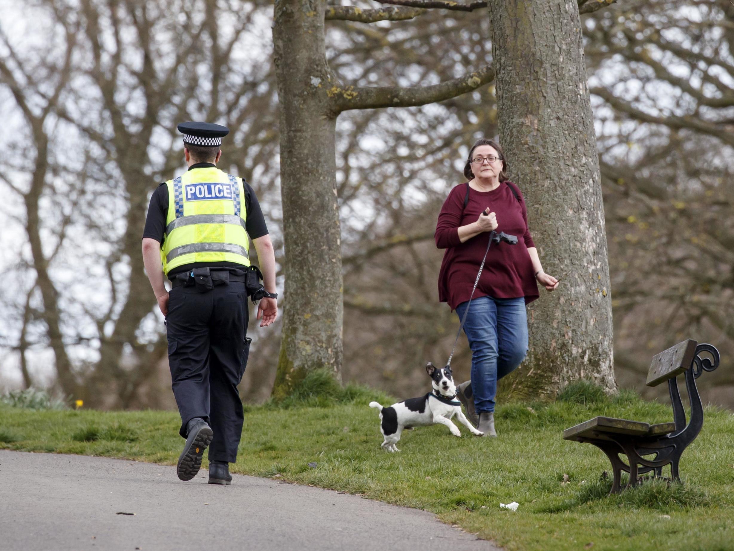A policeman walks past a woman exercising with dog in Roundhay Park, Leeds