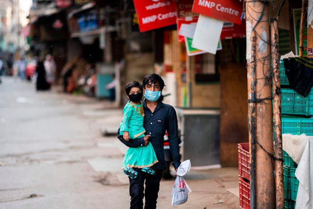 A man with a child, both wearing face masks, walk past closed shops in the old city of Delhi on Thursday 9 April