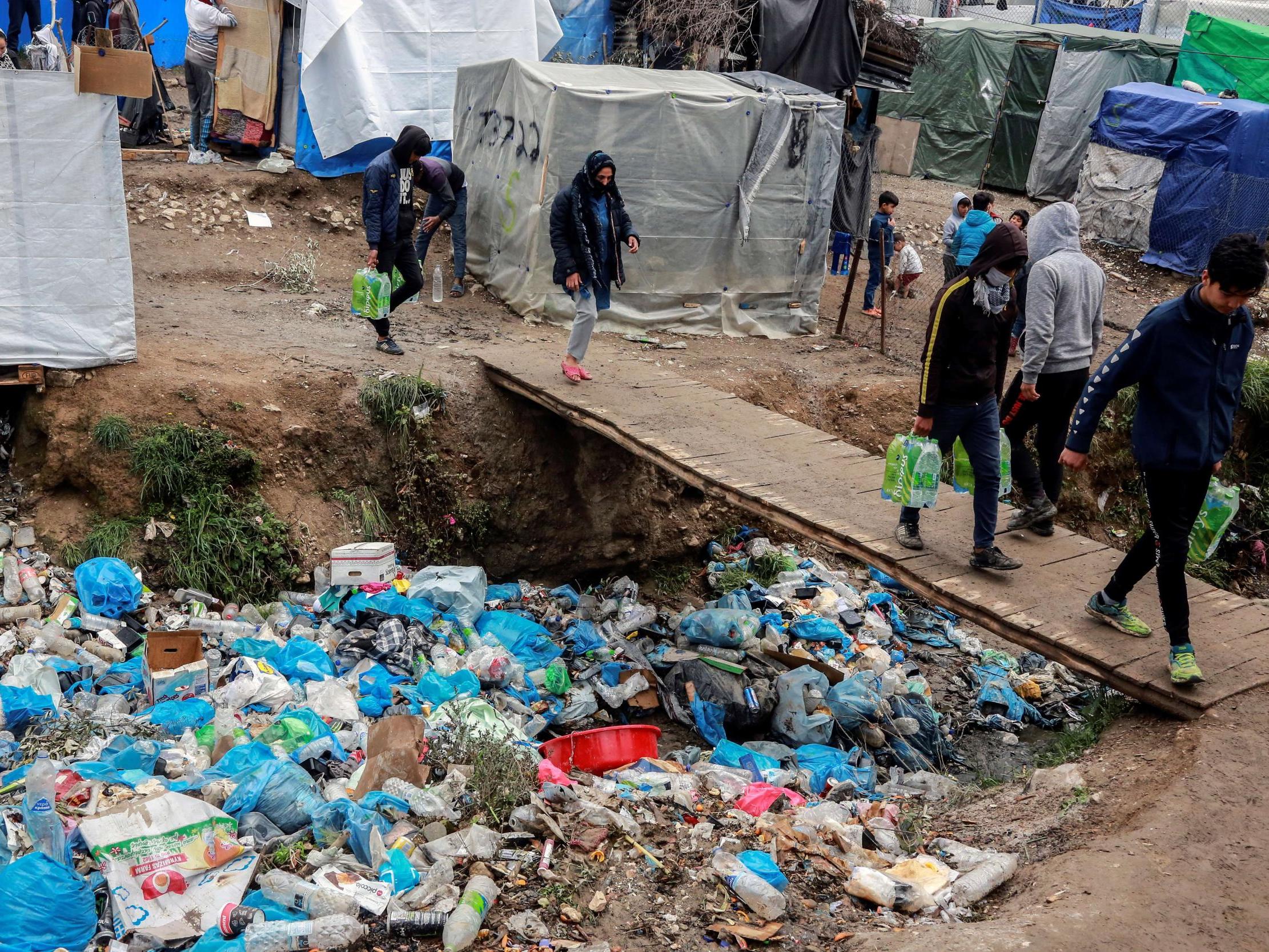 Refugees on the Greek island of Lesbos walk past piles of rubbish