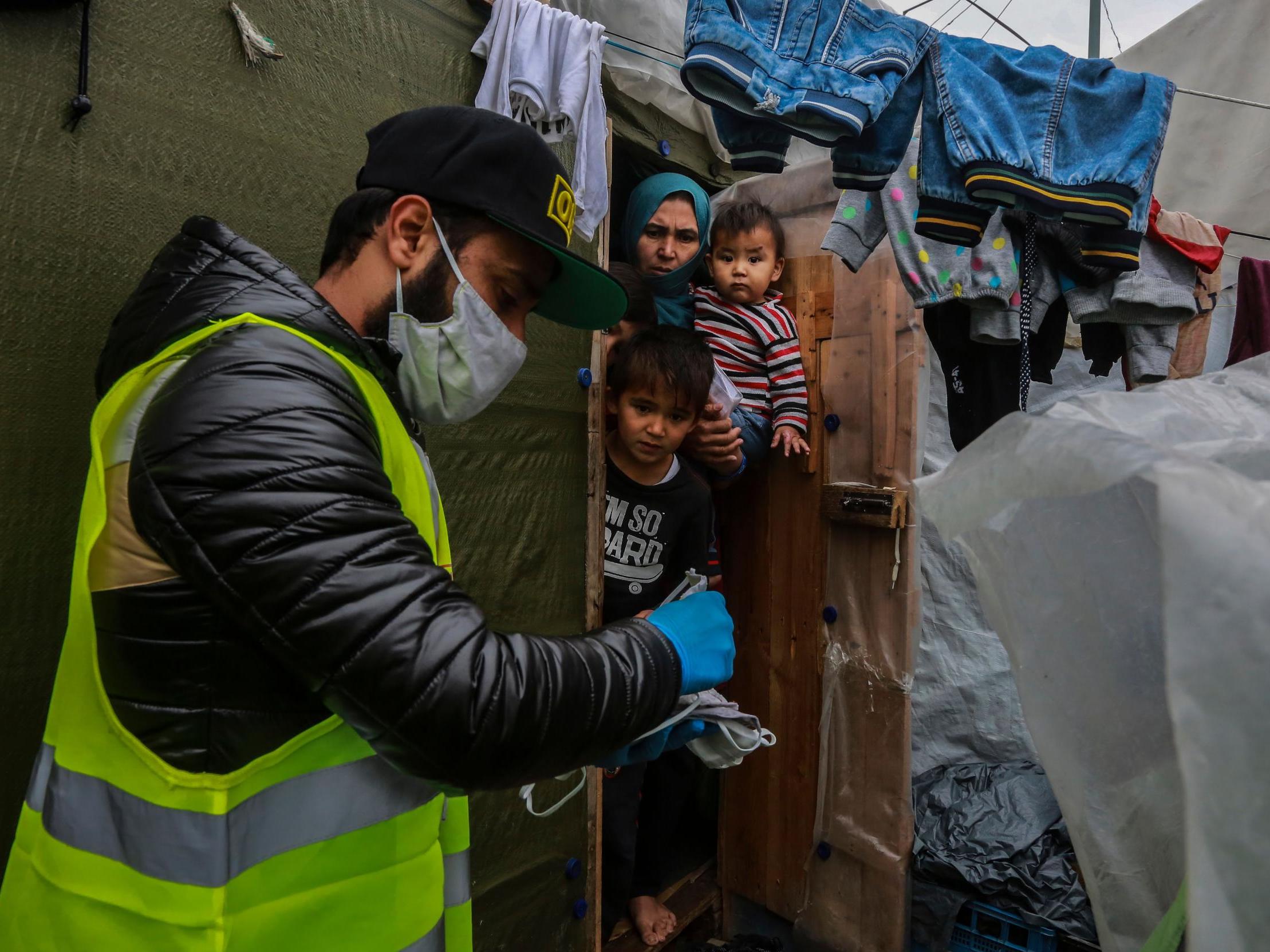 A humanitarian worker provides a refugee family with protective masks in the Greek camp of Moria