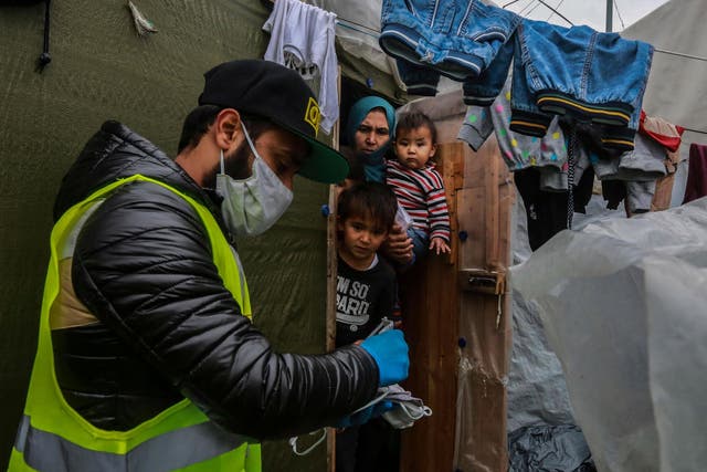 A humanitarian worker provides a refugee family with protective masks in the Greek camp of Moria