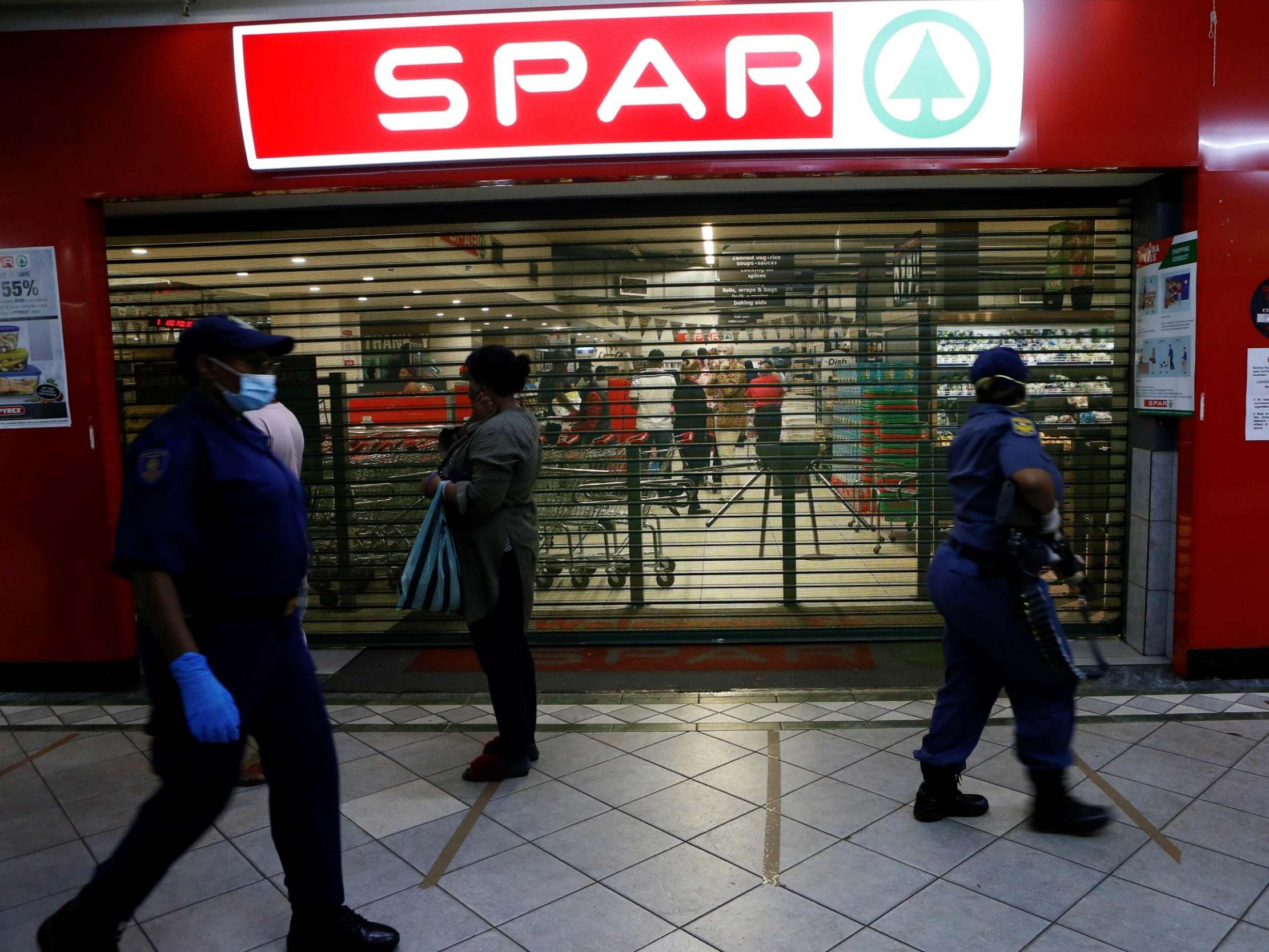 South African Police Service officers walk past shoppers queuing outside a shop in Sunnyside, Pretoria, 7 April 2020.