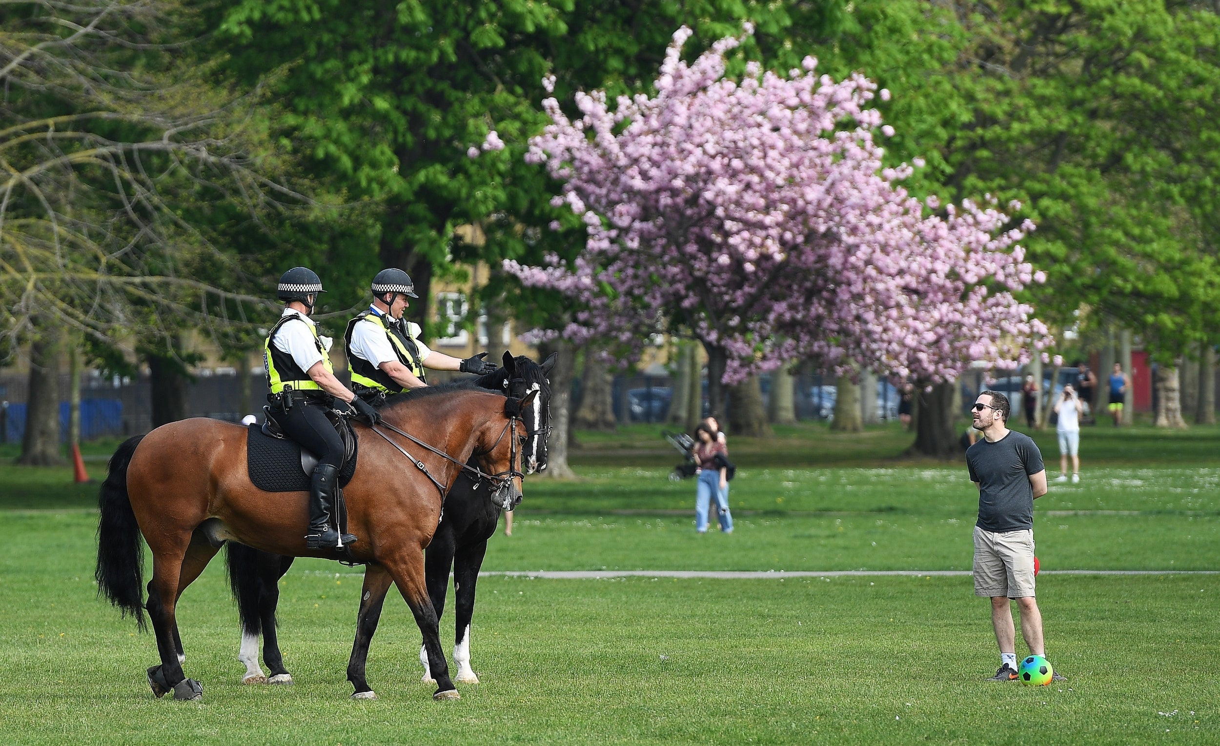 Police on horseback talk to a man in Victoria Park in London, Britain