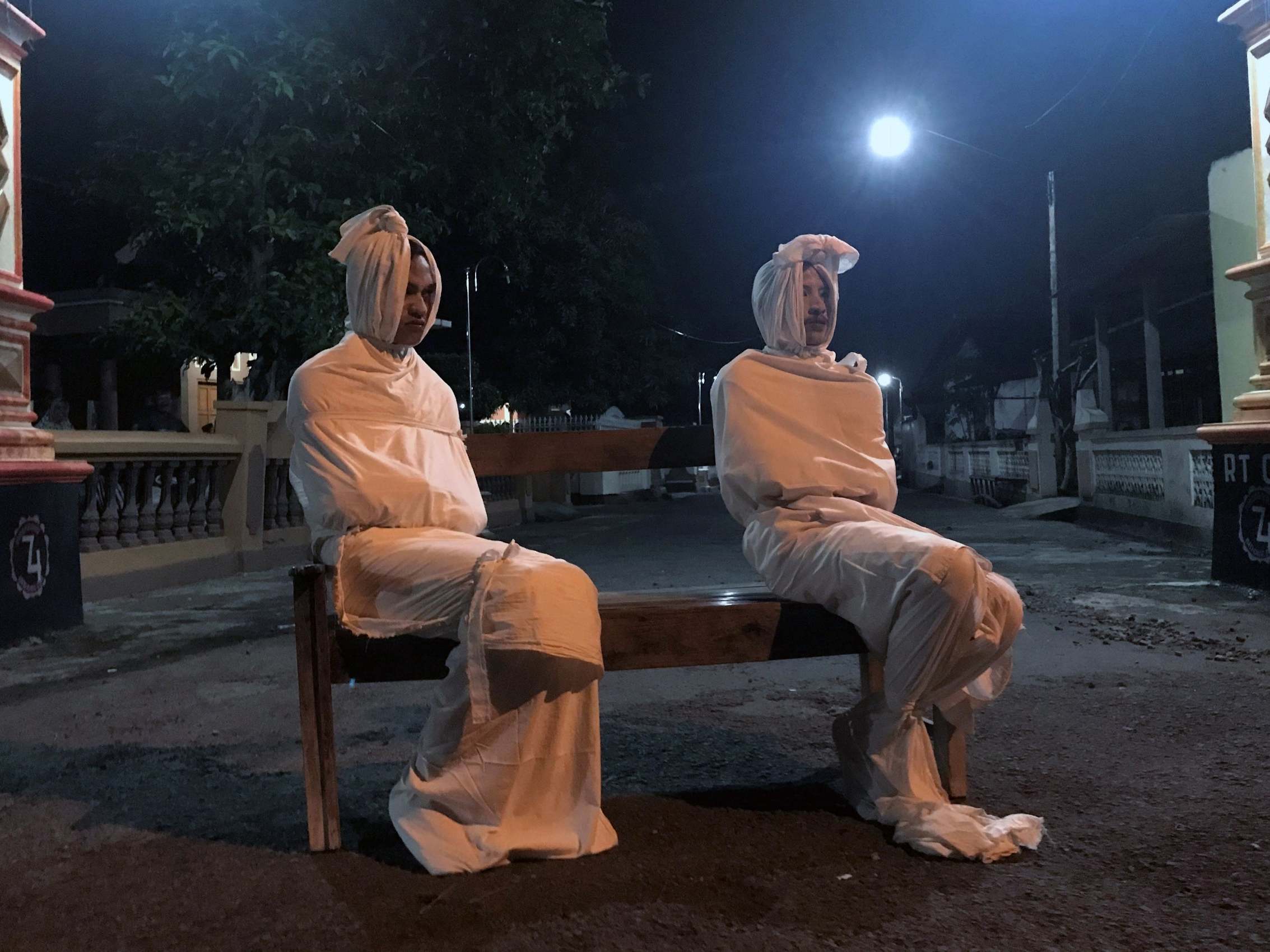 Volunteers Deri Setyawan, 25, and Septian Febriyanto, 26, sit on a bench as they play the role of 'pocong', or known as 'shroud ghost', to make people stay at home amid the spread of coronavirus disease