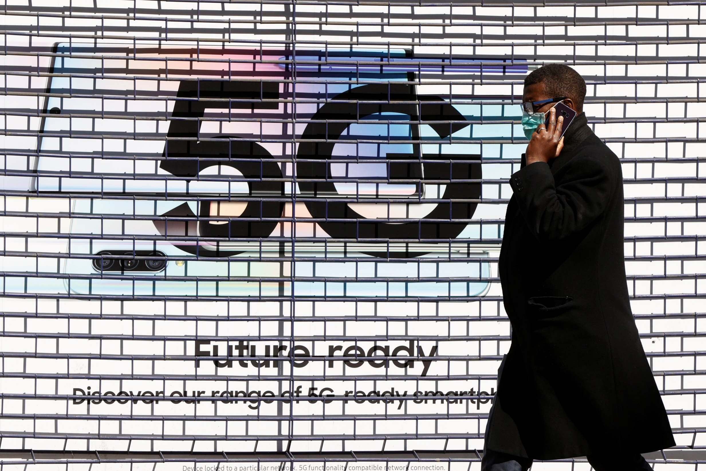 A man wearing a mask walks past a 5G advert in London as the spread of the coronavirus disease continues