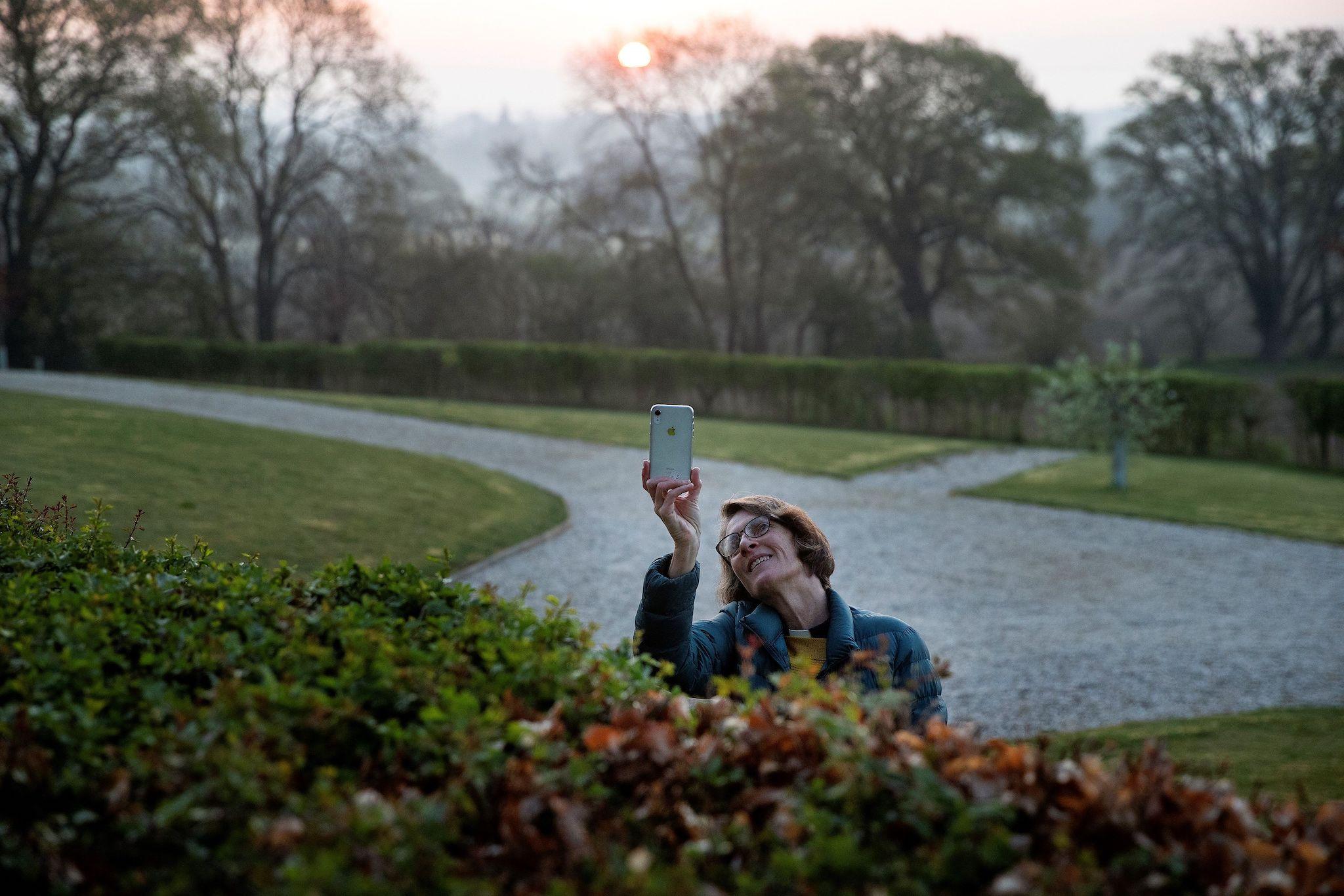 Priest-in-Charge Angie Smith, uses her smartphone to film the sunrise whilst live-broadcasting an Easter Sunday service to her congregation at dawn, from the churchyard of Old St. Mary's Church in Hartley Wintney, west of London, on April 12, 2020