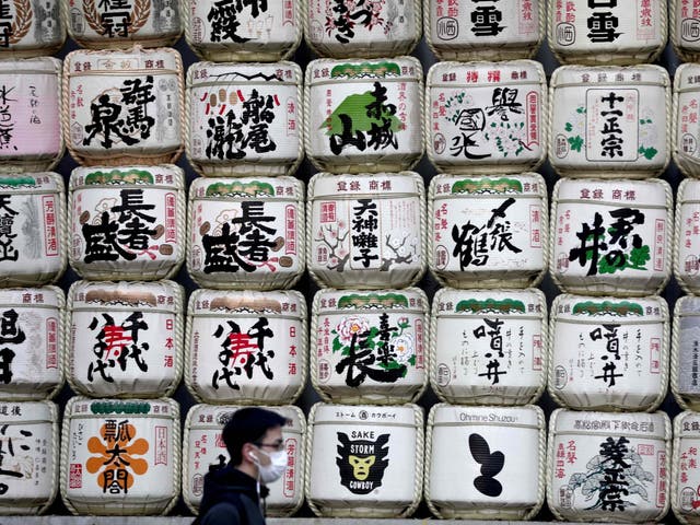 A man wearing a face mask amid concerns over the spread of COVID-19 coronavirus walks past barrels of sake at the entrance of Meiji shrine in Tokyo