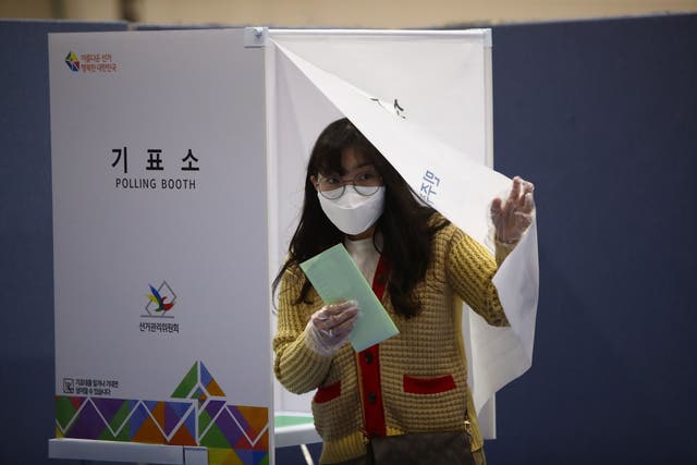 A South Korean woman wearing a mask and plastic gloves casts her vote in the parliamentary election on 15 April amid the coronavirus outbreak