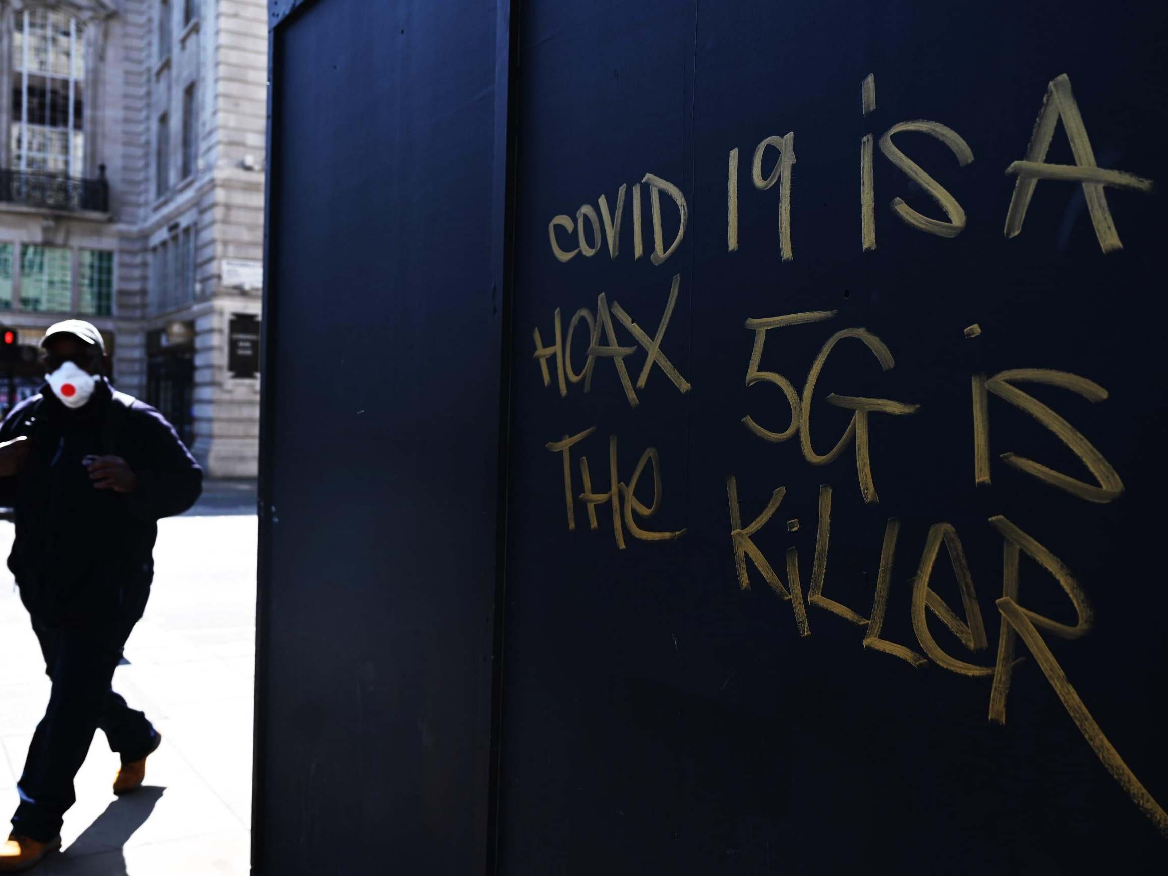 A man in a mask passes 5G conspiracy graffiti in London this week