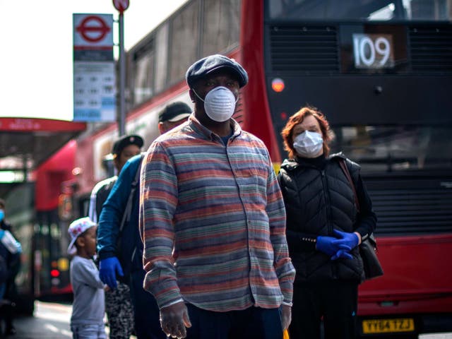 People wearing protective face masks wait in line for a supermarket in Brixton, south London, as the UK continues in lockdown to help curb the spread of the coronavirus, 16 April 2020