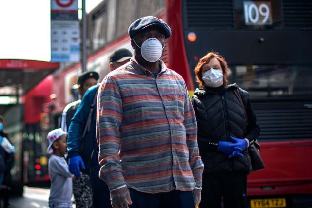 People wearing protective face masks wait in line for a supermarket in Brixton, south London, as the UK continues in lockdown to help curb the spread of the coronavirus, 16 April 2020