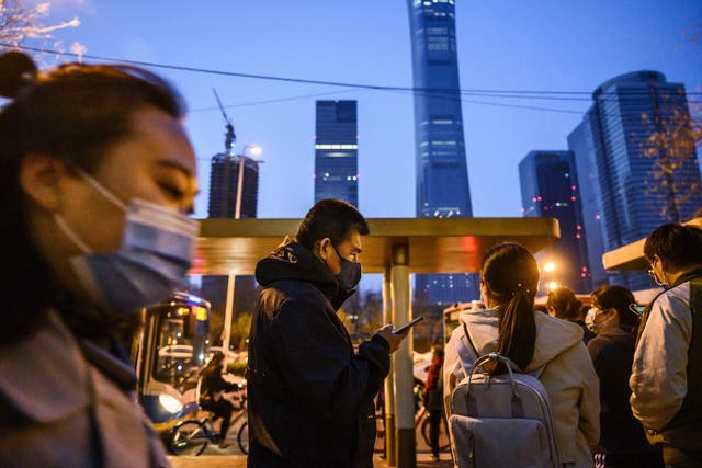 Chinese commuters wear protective masks as they line-up and wait to board a public bus home in the central business district during rush hour on Beijing, China