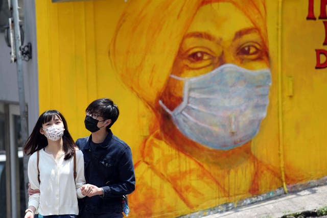 People walk by a painting of a woman wearing a face mask amid the coronavirus (COVID-19) outbreak in Hong Kong