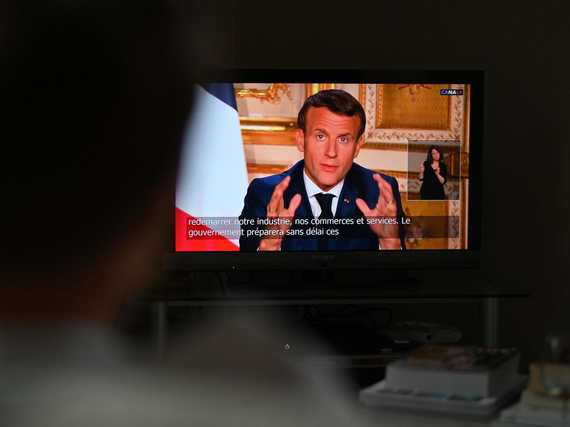 A spectator watches TV in Paris, as French President Emmanuel Macron speaks from the Elysee Palace during a televised address to the nation on 13 April