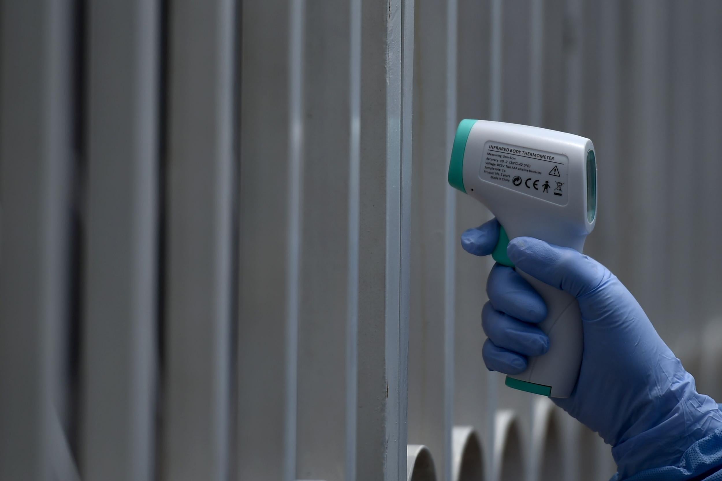 A health worker wearing a biosafety suit takes the temperature of a man through the railings during a checkup for the novel coronavirus