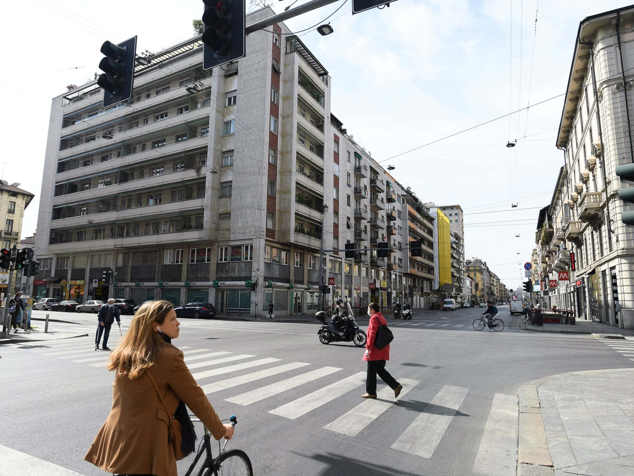 People wearing protective masks cross a street as the number of people walking outside in the city increases