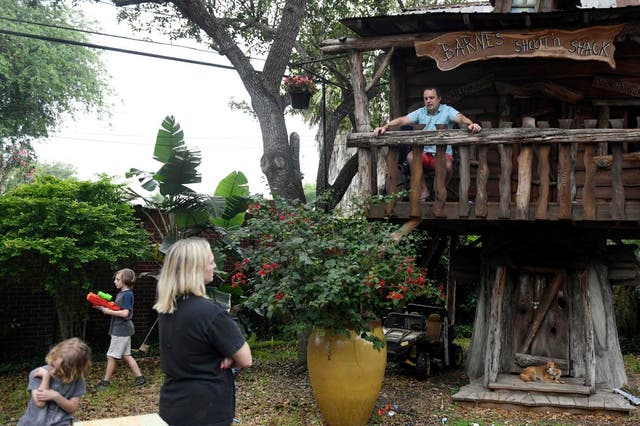 Barnes, top right, sits in his kids' treehouse while his family plays in their backyard in Corpus Christi, Texas