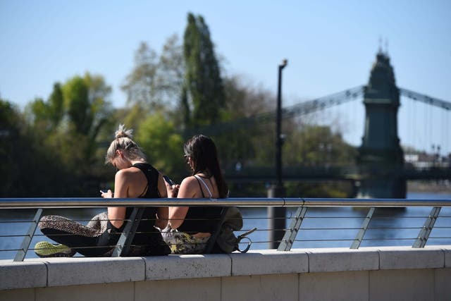 Two women sit in the sun on the Thames path near Hammersmith Bridge, London