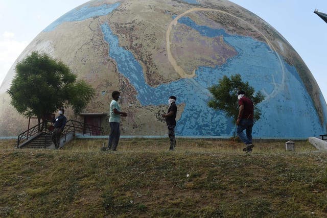 Staff members of the the Gujarat Science City wearing facemasks stand in front of a planet earth model on the eve of World Earth Day at Gujarat Science City