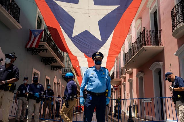 Puerto Rico police officers stand in front of the governor's mansion as hundreds of private and municipal paramedics protest in their ambulances through Old San Juan