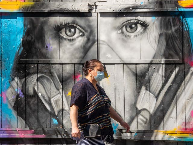 A woman passes a mural showing a woman wearing a face mask, in Shoreditch, east London