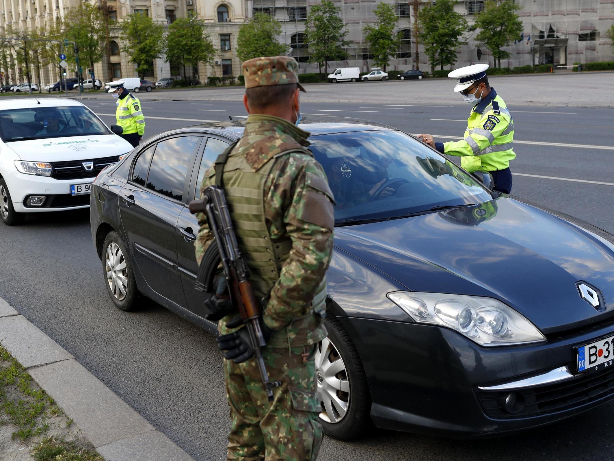 Romanian policemen check the papers of two car drivers as an armed military man (C) watches the scene in downtown Bucharest, Romania, on 20 April 2020.