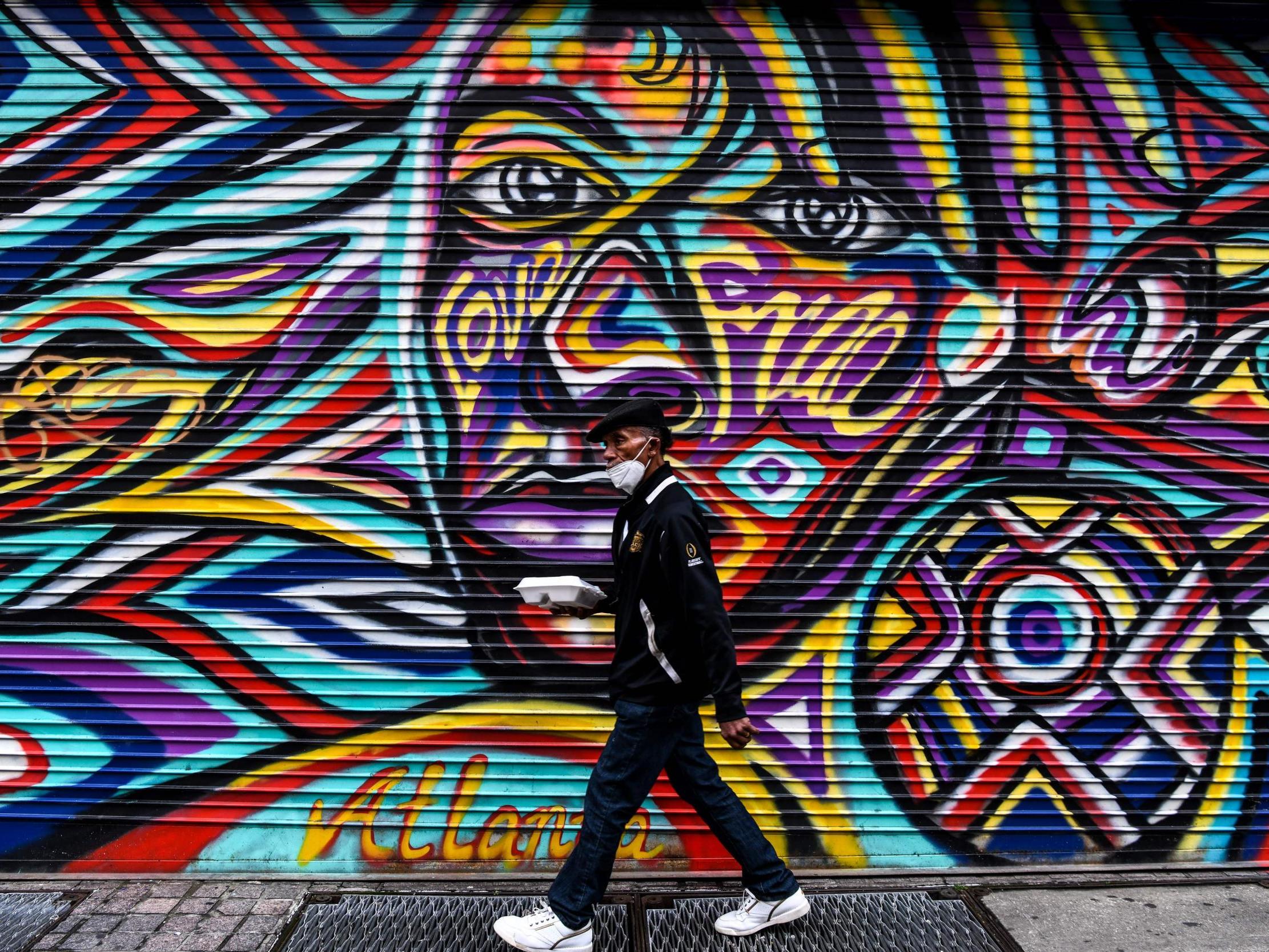 A man wears a mask as he walks past a mural in downtown in Atlanta, Georgia