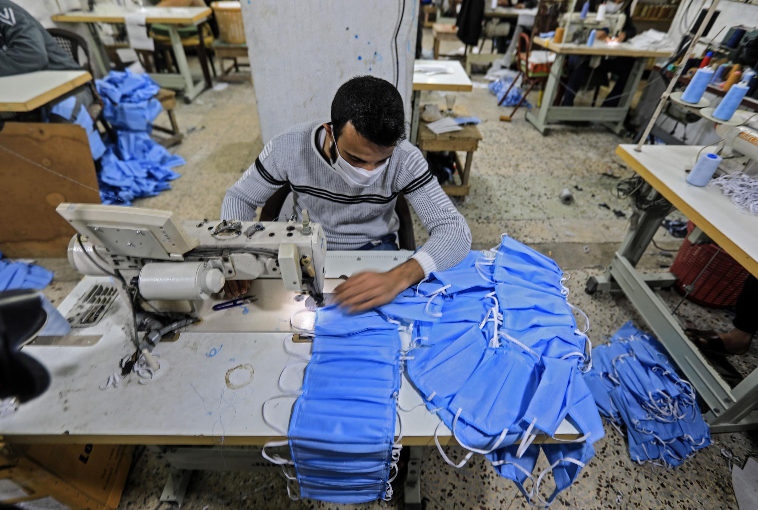 Palestinian workers manufacture protective coverall suits and masks at a workshop in Gaza City on March 30, 2020 amid coronavirus COVID-19 pandemic
