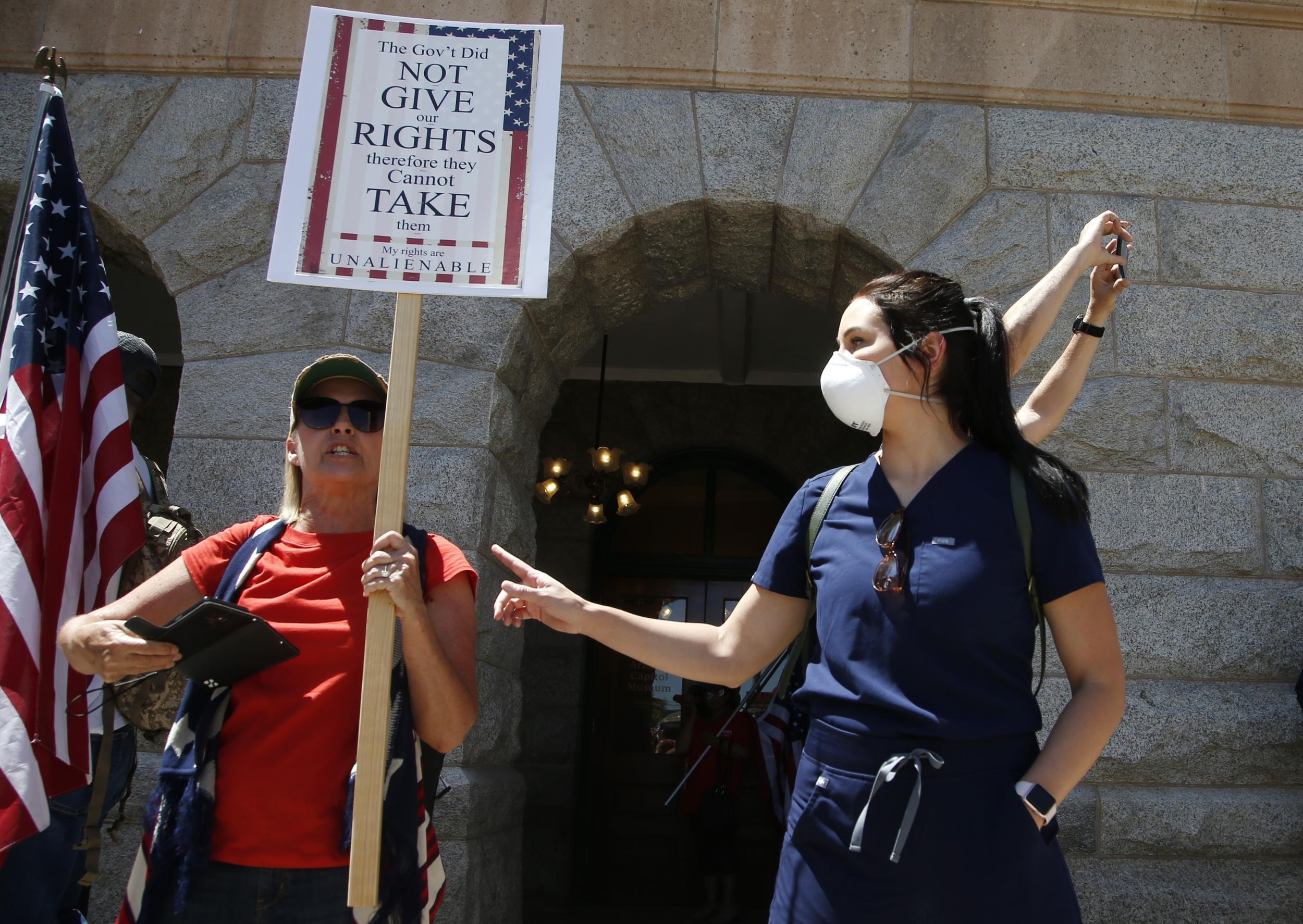 A local caregiver counter protester, right, points to a protester to keep a safe social distance at a rally at the capitol to 're-open' Arizona against the governor's stay-at-home order due to the coronavirus Monday, April 20, 2020, in Phoenix. (AP Photo/Ross D. Franklin)