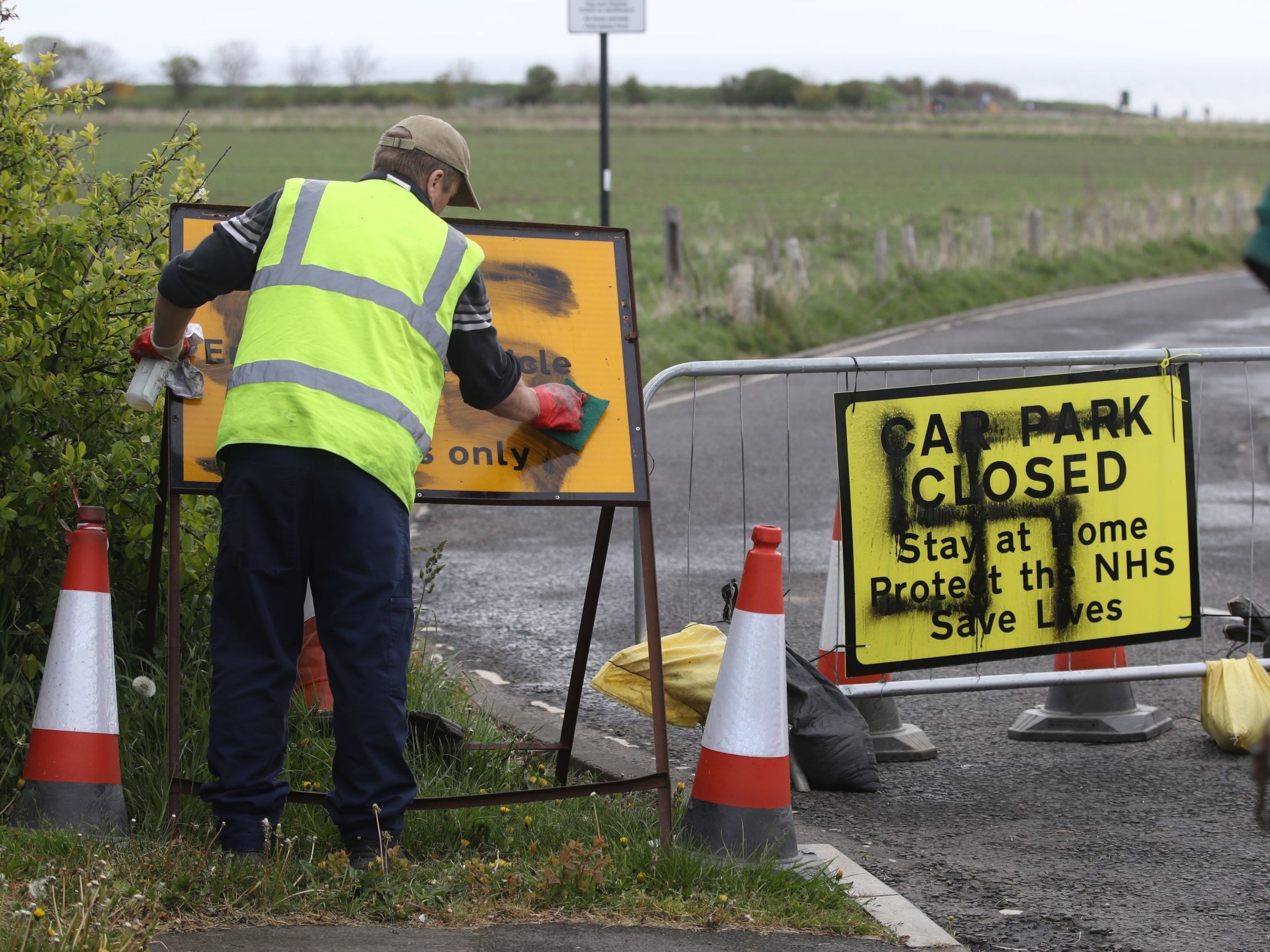 A worker removes a swastika spray painted on a sign at the entrance to a closed road and car park near Whitley Bay lighthouse, North Tyneside, 30 April 2020.
