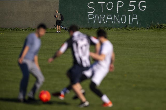 People play football in front of graffiti reading ‘Stop 5G Paranoia’ painted on a wall in east London on 19 April 2020