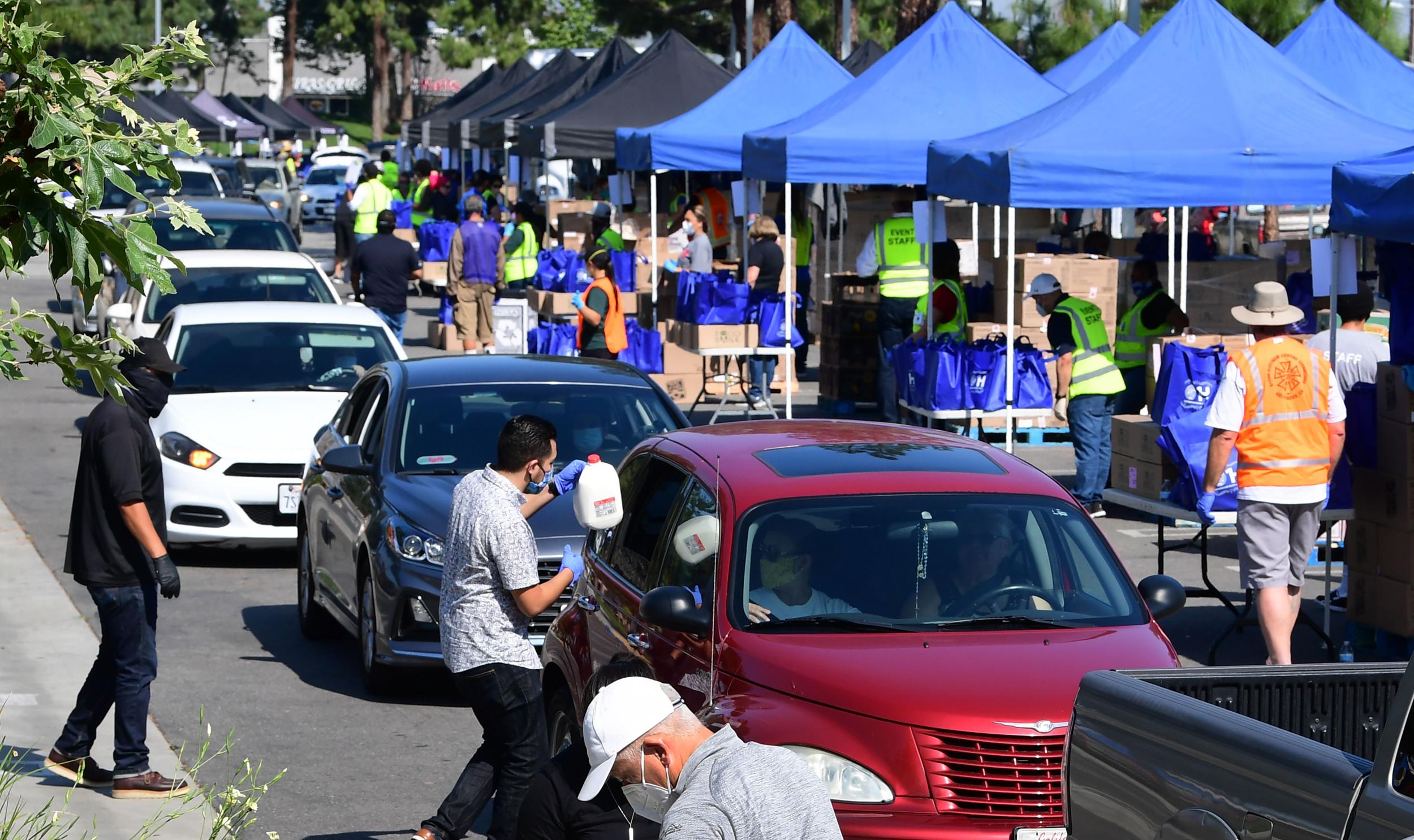 Volunteers help load food as vehicles arrive at a Los Angeles Regional Food Bank drive-thru giveaway in Pico Rivera, California on April 28, 2020. - An estimated 3,000 families are facing food and/or economic difficulties due to the COVID-19 pandemic as California processes 3.2 million unemployment claims since March 15. (Photo by Frederic J. BROWN / AFP) (Photo by FREDERIC J. BROWN/AFP via Getty Images)