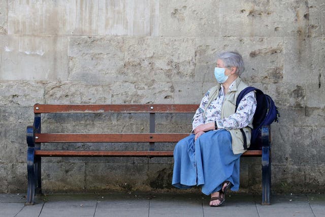 A member of the public wears a face mask as she sits on a bench