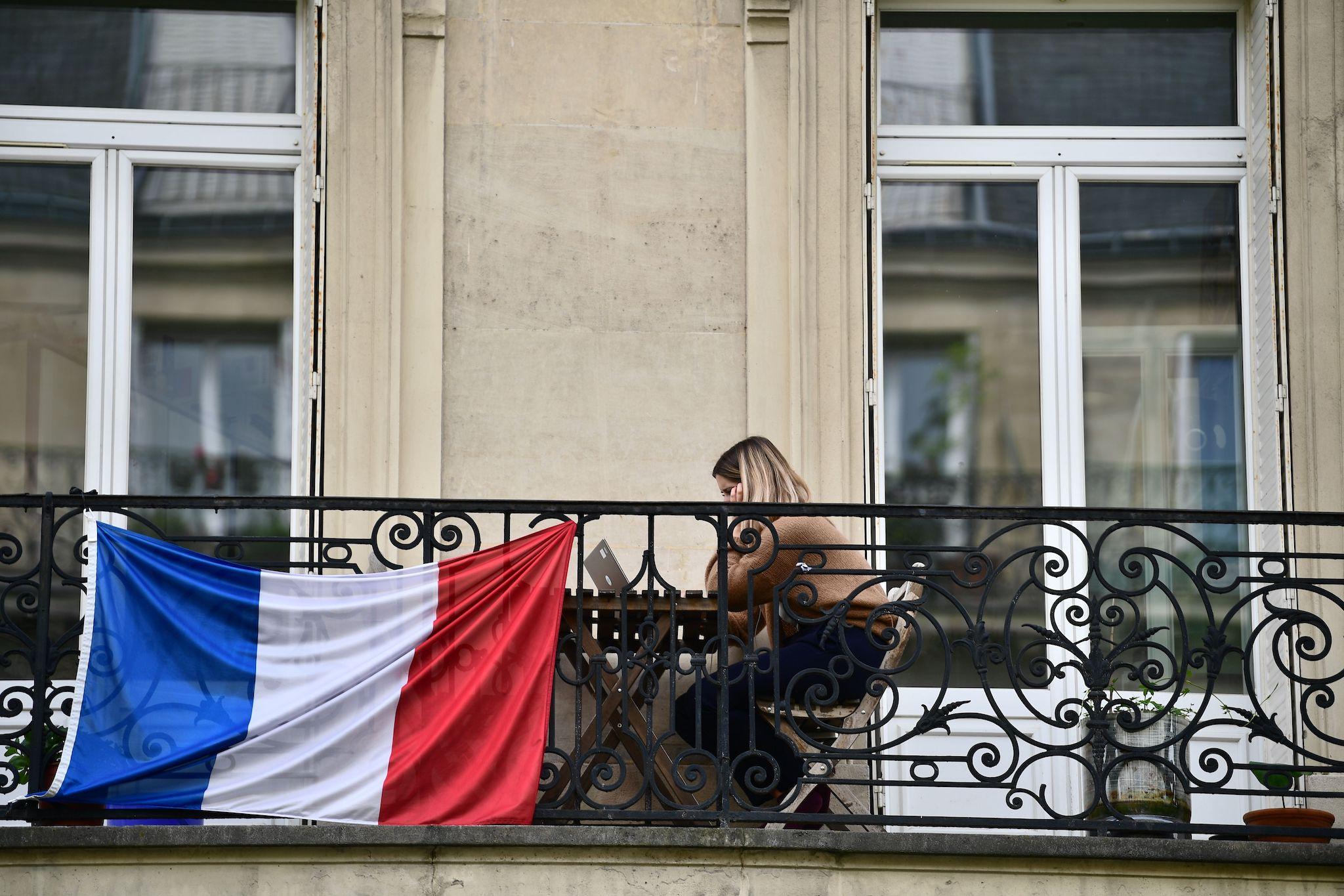 A woman sits on her balcony looking at her laptop in Paris on April 17, 2020, on the 32nd day of a lockdown across France aimed at curbing the spread of the COVID-19 pandemic, caused by the novel coronavirus