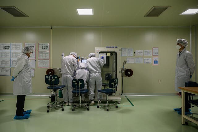 Staff members monitor a machine dispensing Covid-19 novel coronavirus antigen and antibody diagnostic material onto a membrane