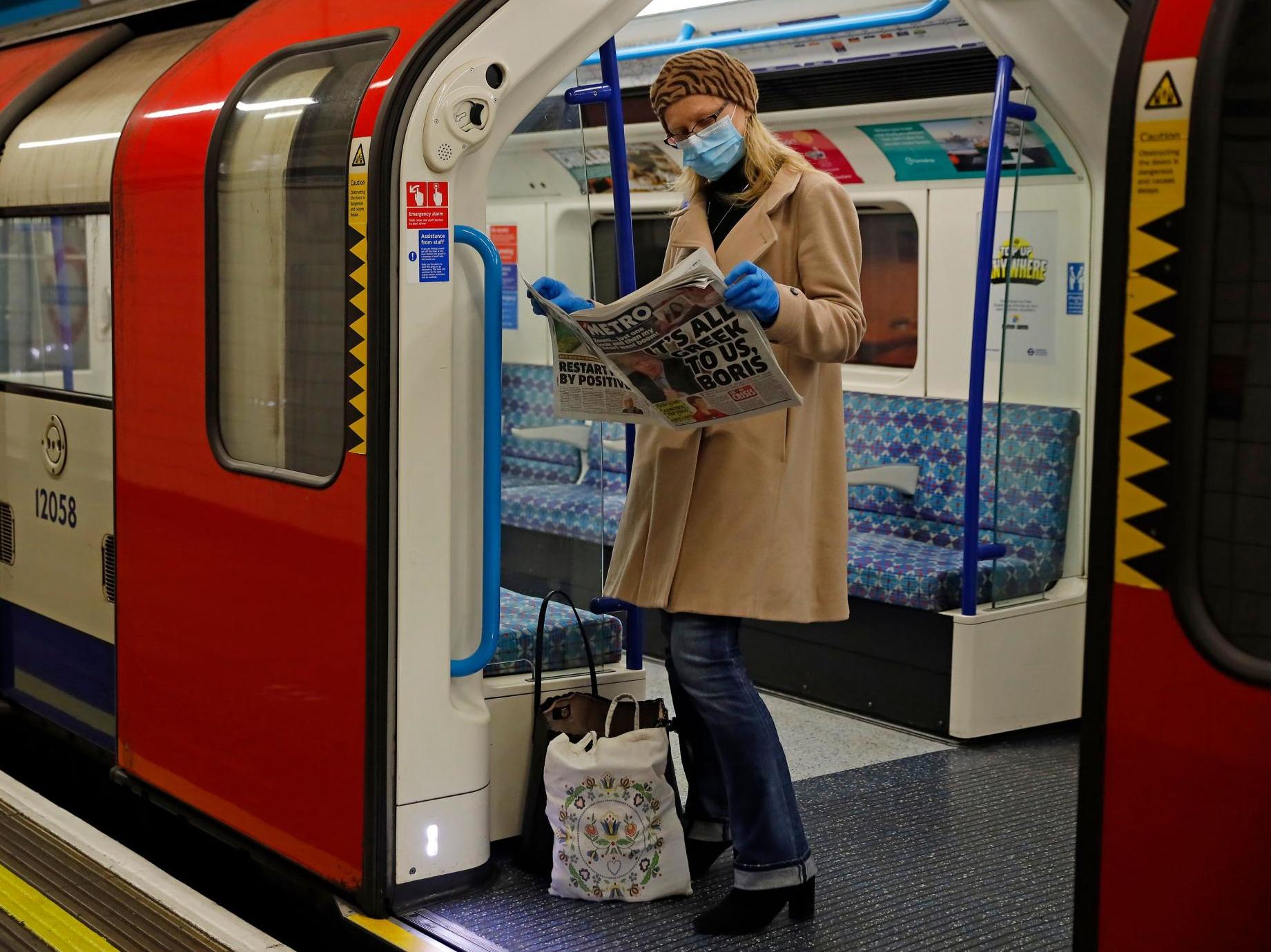 A woman wearing PPE reads a newspaper on the London Underground yesterday