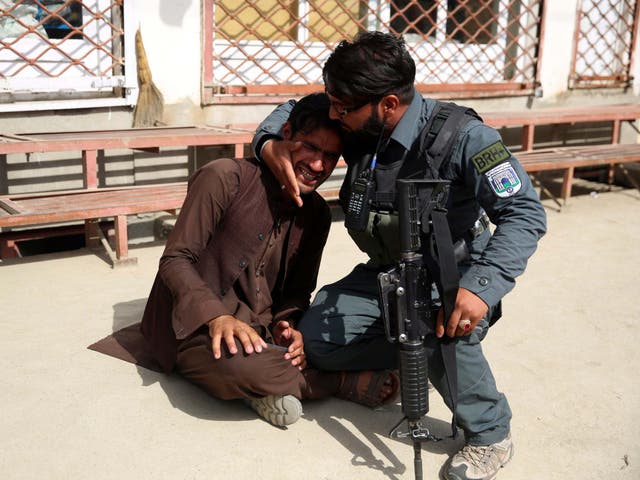 Afghan policeman comforts a man after an attack on a maternity hospital, in Kabul, Afghanistan, Tuesday, May 12, 2020