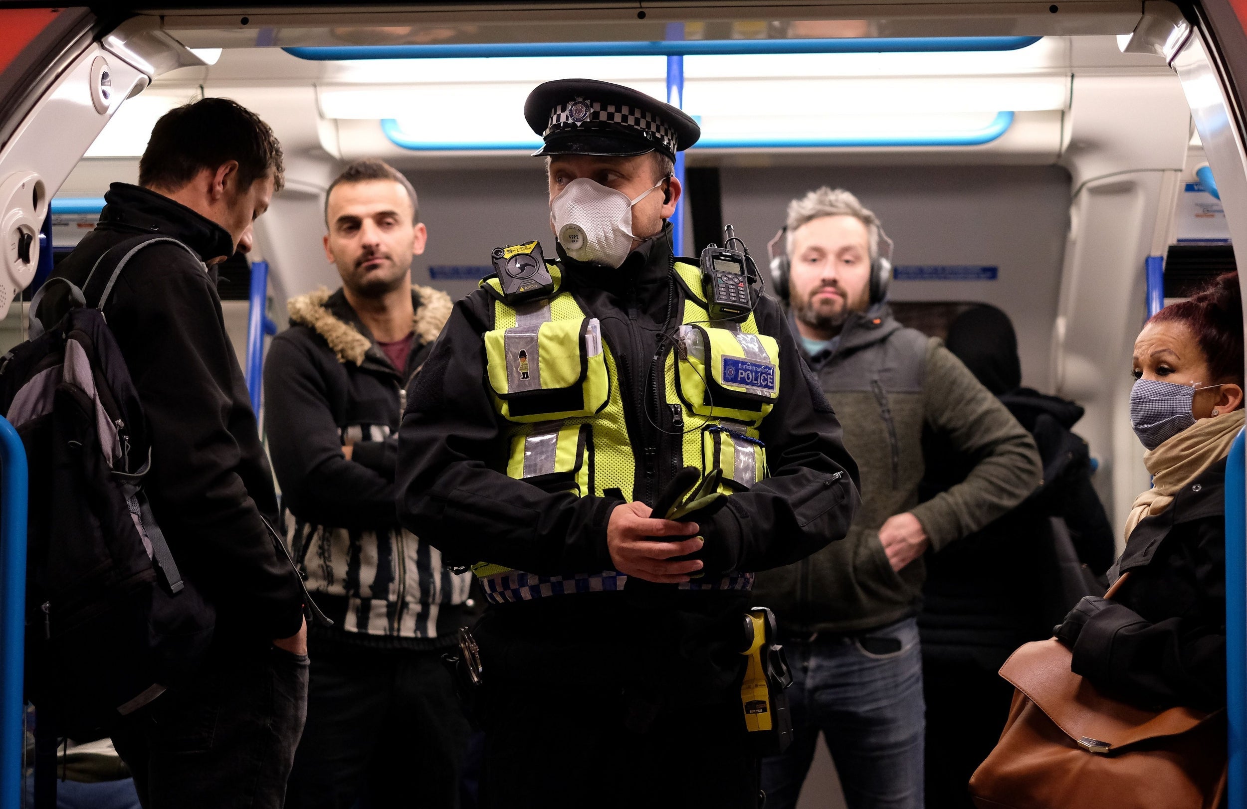 A police officer wearing PPE stands with commuters as they travel in the morning rush hour on TfL