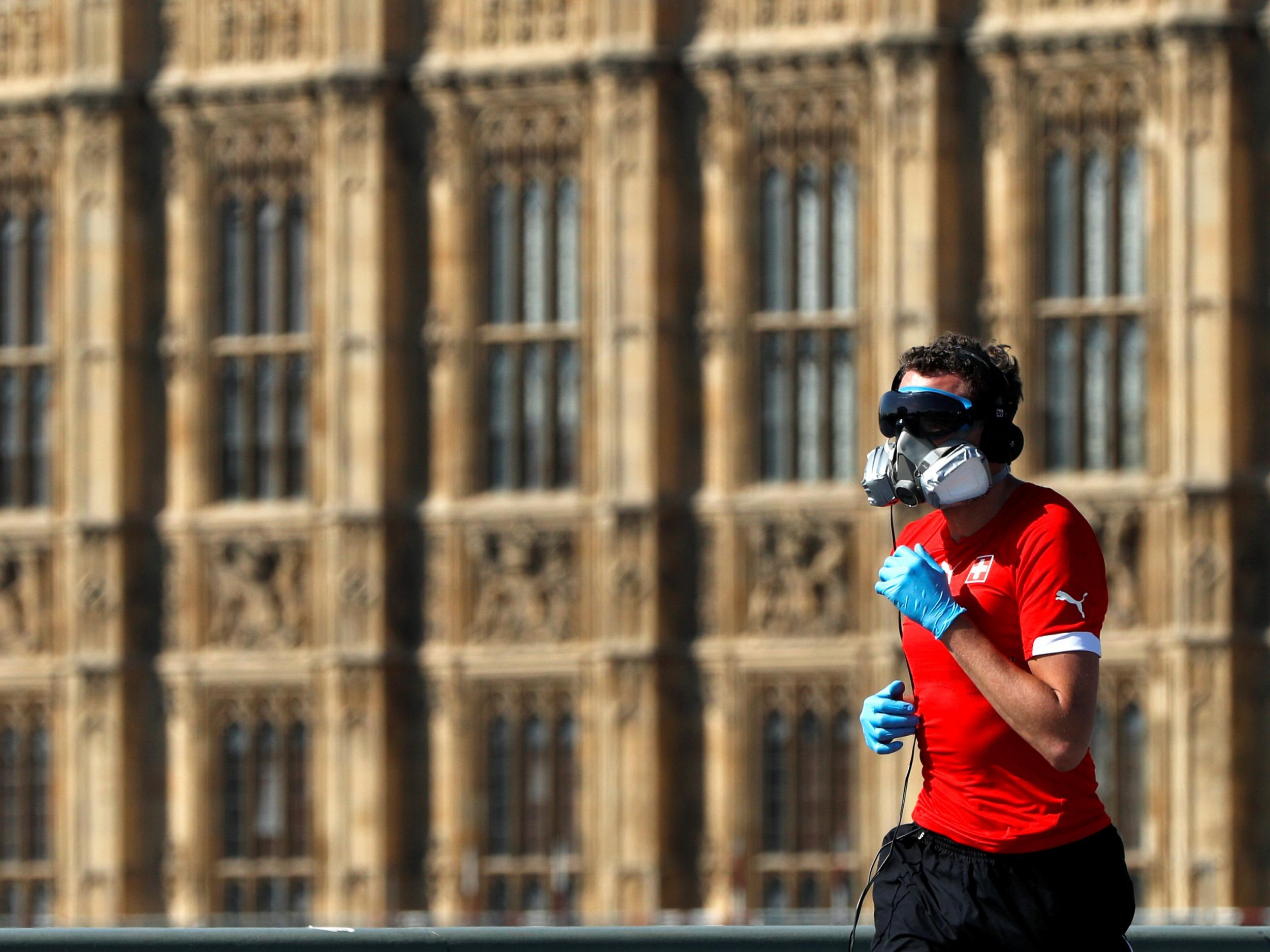 A runner wearing a gas mask, eye protection and gloves jogs over Westminster Bridge in London, 23 April, 2020.