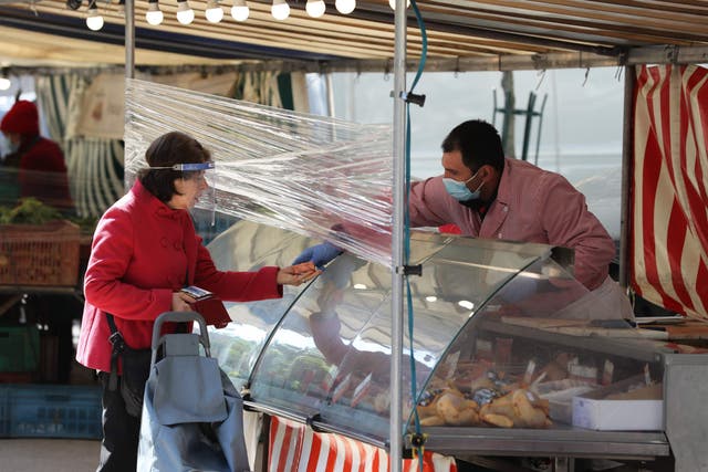 A shopper wearing a visor buys products from a butcher's stall at a street market in Paris
