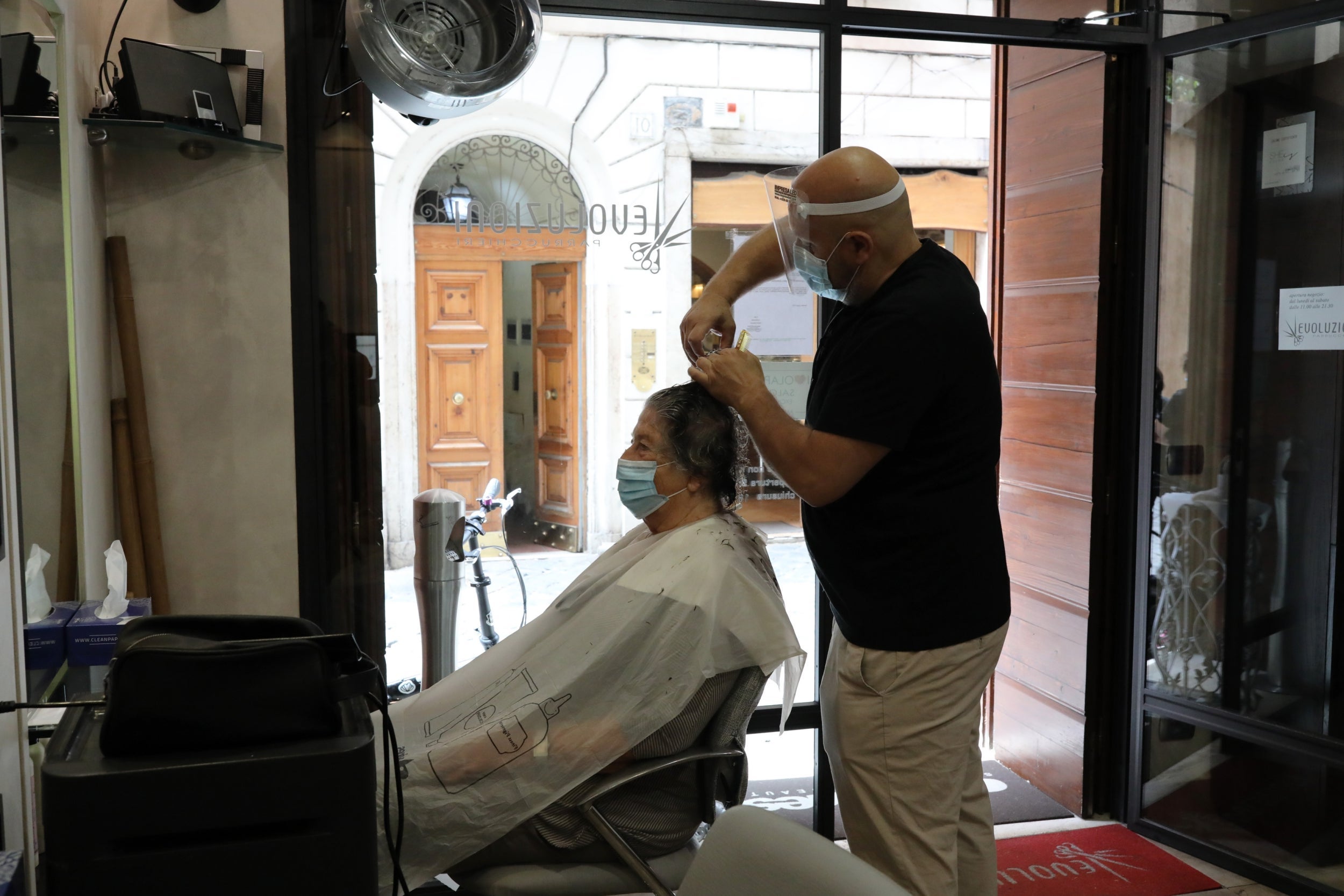 A hairdresser in Rome cuts a woman’s hair using all the protective devices prescribed by regulations