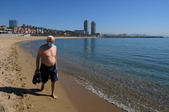 A man wearing a face mask walks at Barceloneta beach in Barcelona today