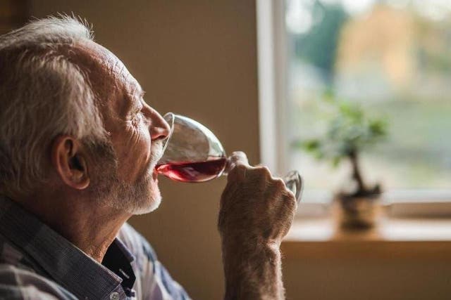 A man drinks red wine at home while looking out of the window